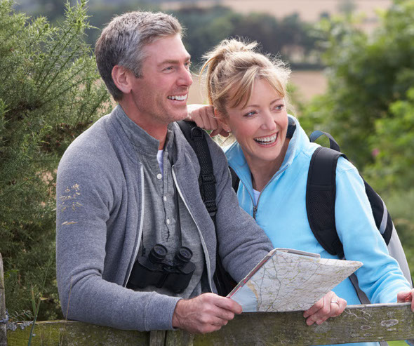 Middle-age man and women are hiking on a sunny country path while looking at a map for directions.