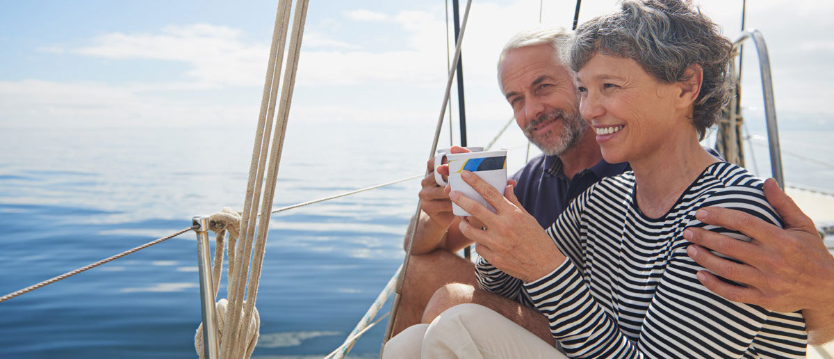 Photo of a retired couple drinking coffee while enjoying the day on their sailboat.