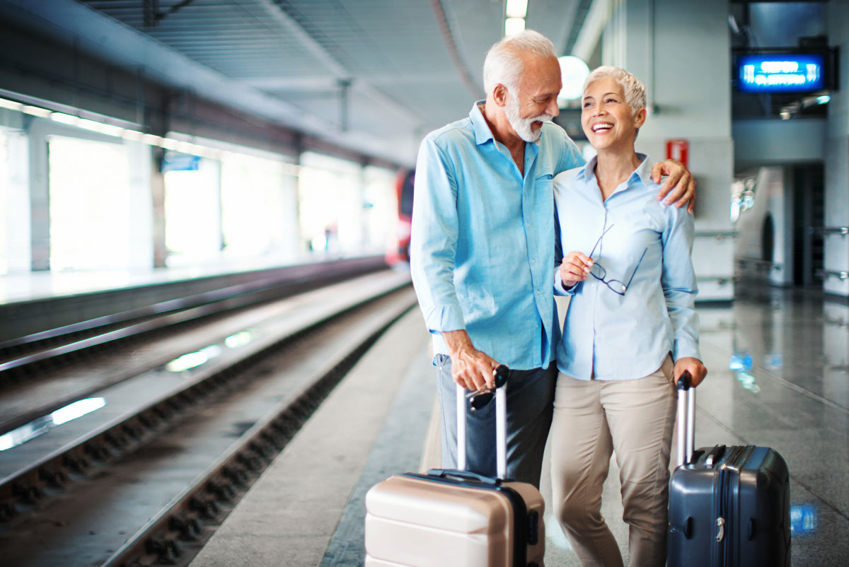 Photo of a retired couple in a train station enjoying travelling together.